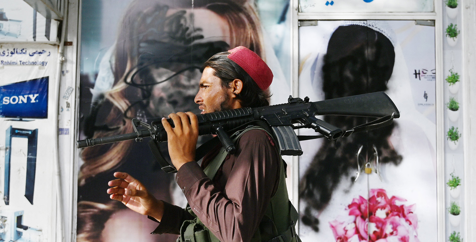 Taliban fighter walks past a beauty salon with images of women defaced using spray paint